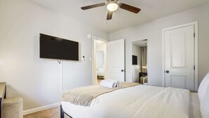 Ein Schlafzimmer mit Bett, Deckenventilator, Fernseher und einer Tür zu einem anderen Raum.
