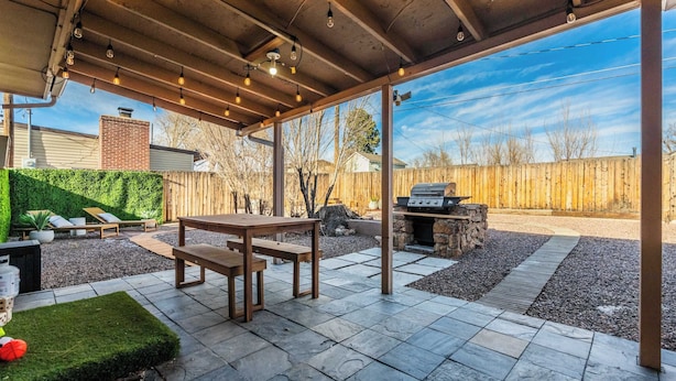 Eine Außenpatio mit Holztisch und -bänken, einem Grill und einer grünen Wand.