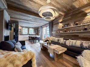 L’intérieur d’une cabane en rondins moderne présente un espace de vie chaleureux, un plancher en bois, un coin repas et une cuisine visible à travers une porte ouverte.
