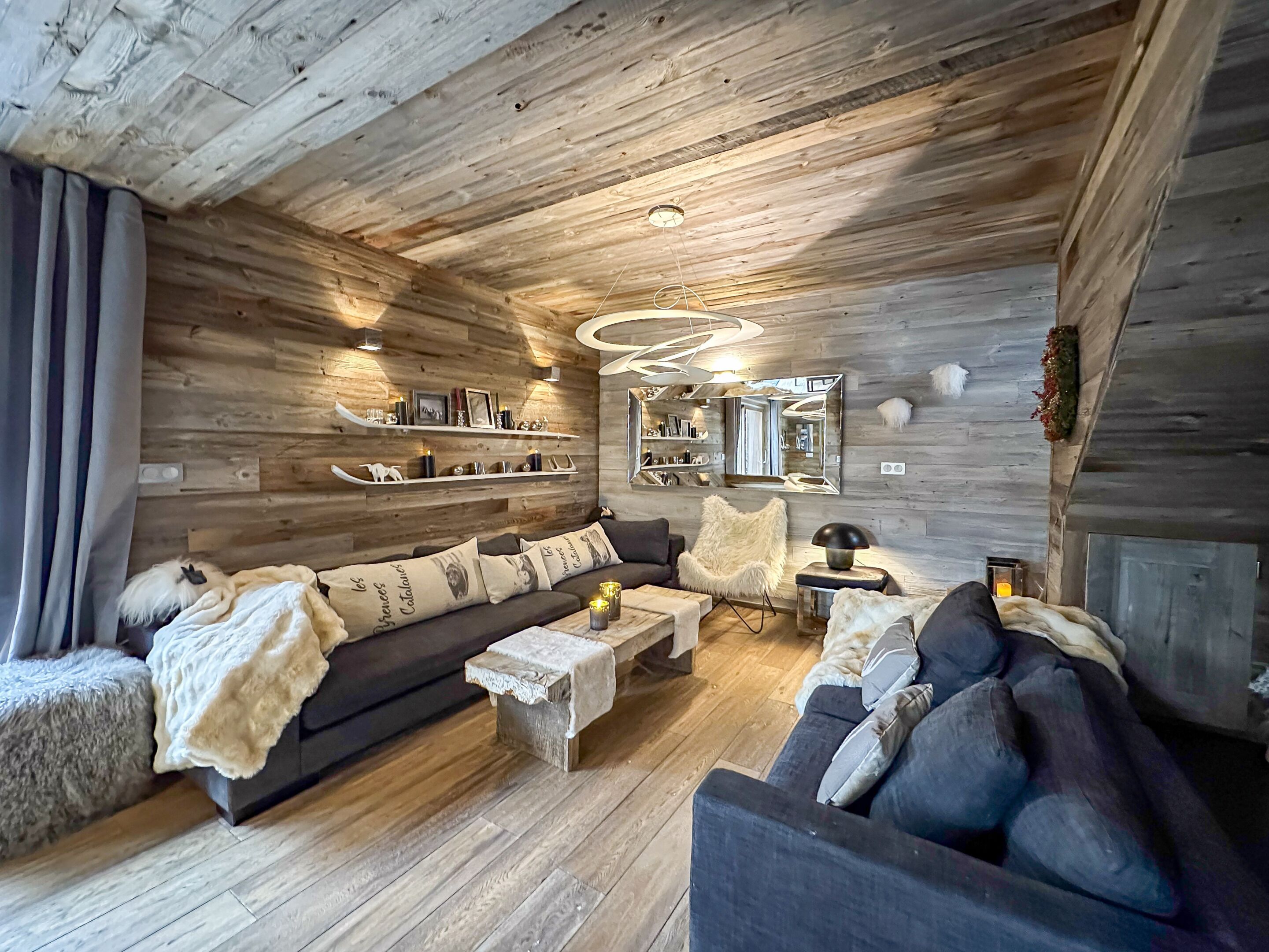 A cozy living room with a wooden ceiling, a sofa set, a coffee table, and a fluffy chair.