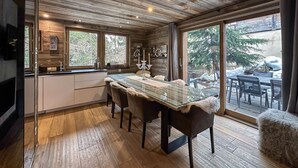 A wooden cabin interior with a dining area, large windows, and a view of the outdoors. - Chalet-Nashira-Deluxe-Private Bathroom-Terrace (Bolquère)
