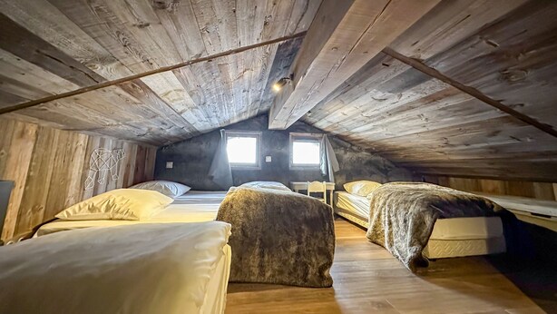 An attic bedroom with wooden beams, two beds, a small table, and a window providing natural light. - Chalet-Nashira-Deluxe-Private Bathroom-Terrace (Bolquère)