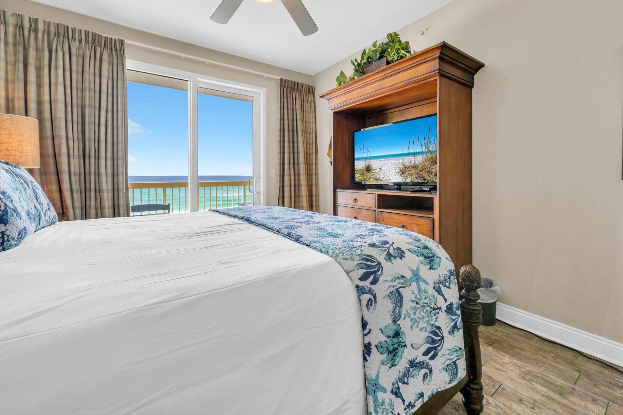 Une chambre d’hôtel avec un grand lit, une télévision, une armoire en bois et un balcon avec vue sur l’océan.