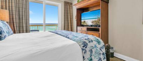 Une chambre d’hôtel avec un grand lit, une télévision, une armoire en bois et un balcon avec vue sur l’océan.
