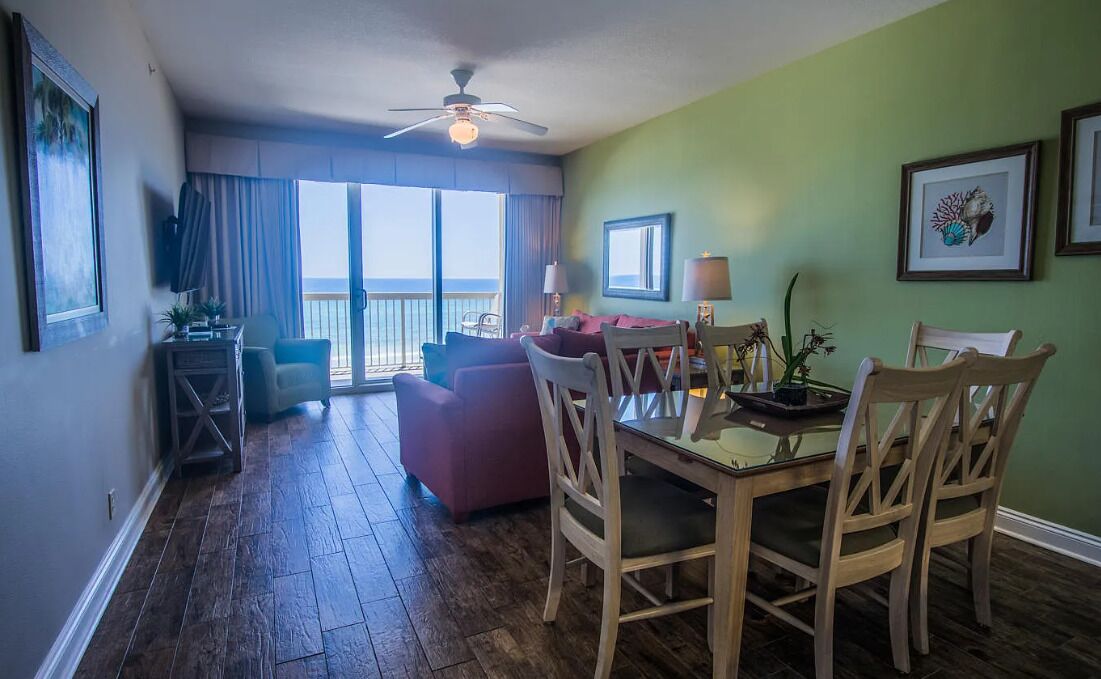 A dining area with a table and chairs, a sofa, and a balcony with a view.