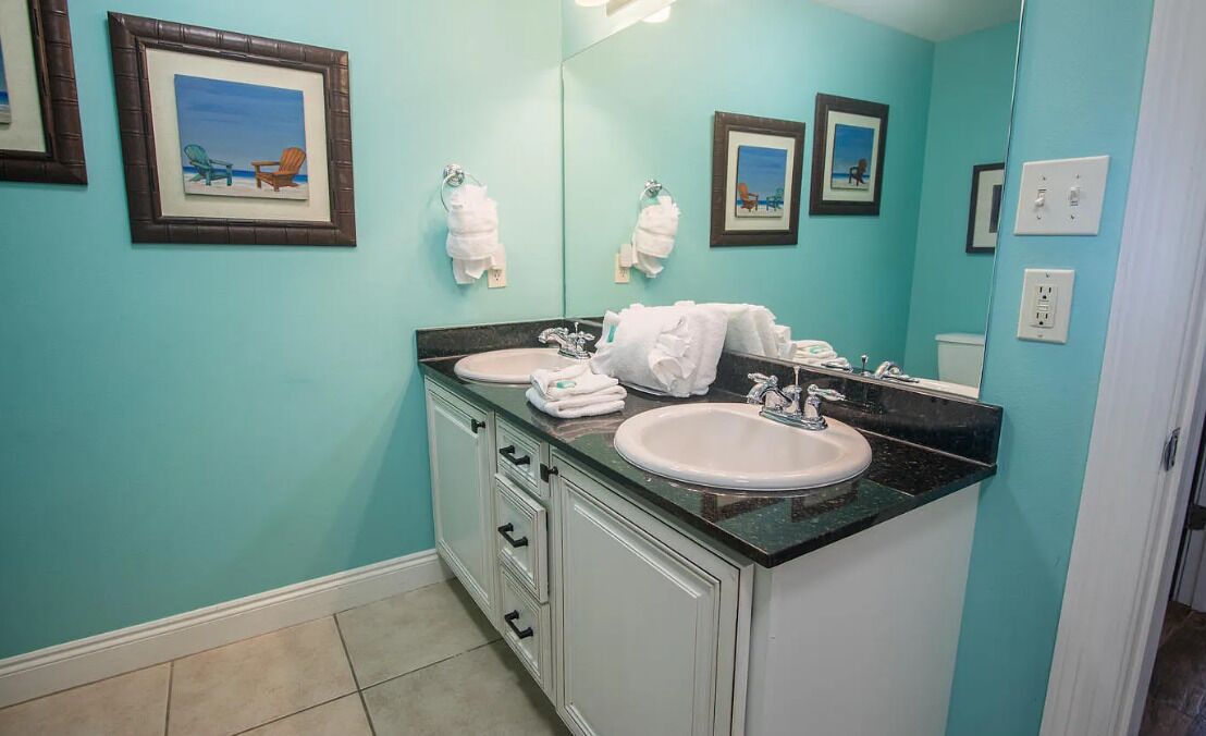 A bathroom with two sinks, a large mirror, and artwork on the walls.