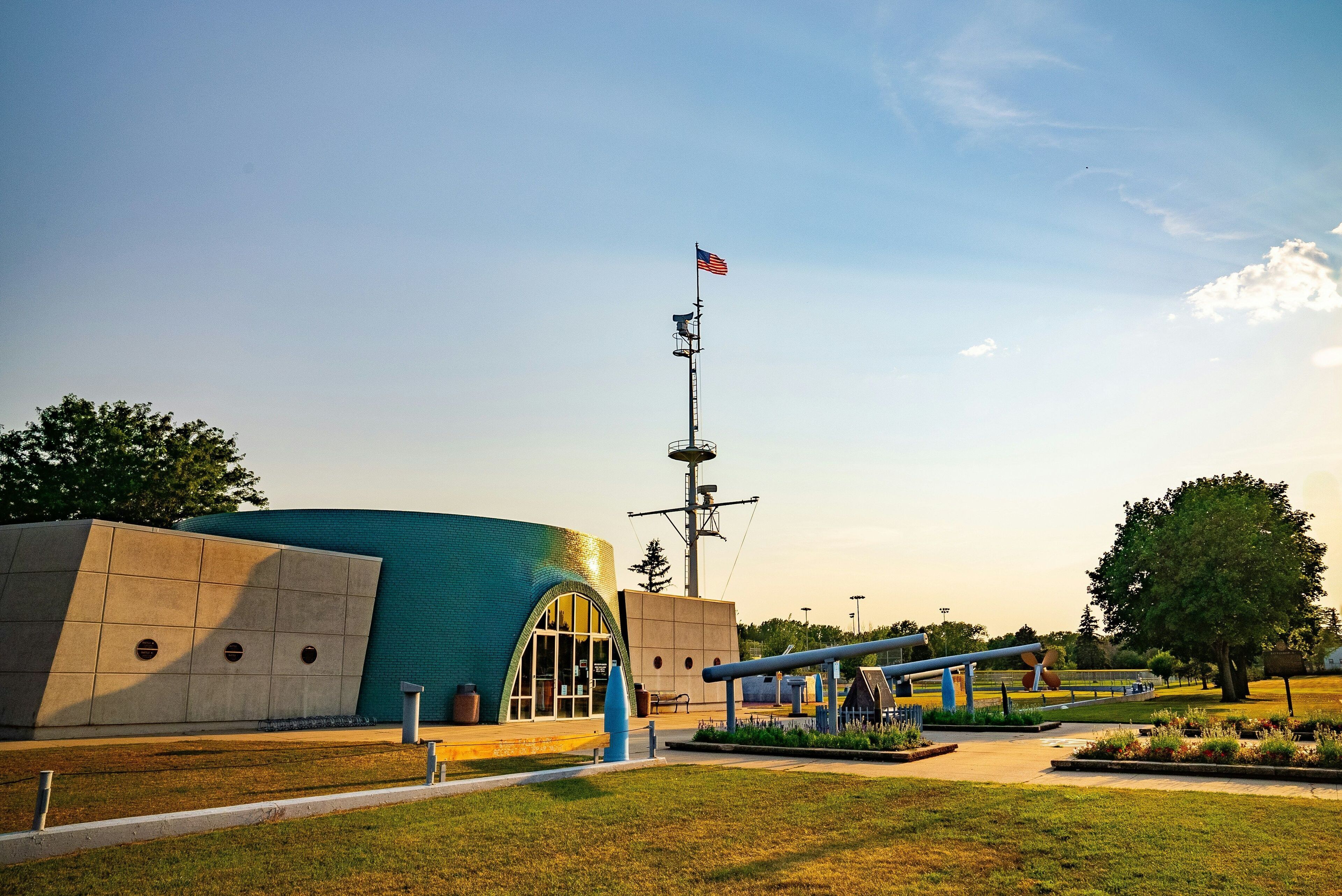 A building with a large arched entrance, a flagpole with an American flag, and a blue structure in the background.