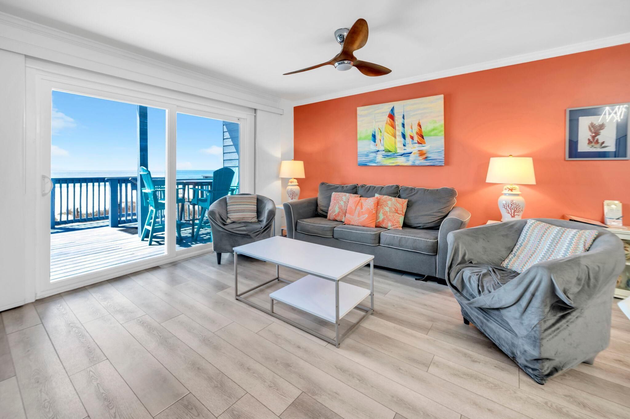 A living room with a balcony, a grey sofa, a white coffee table, and a ceiling fan.