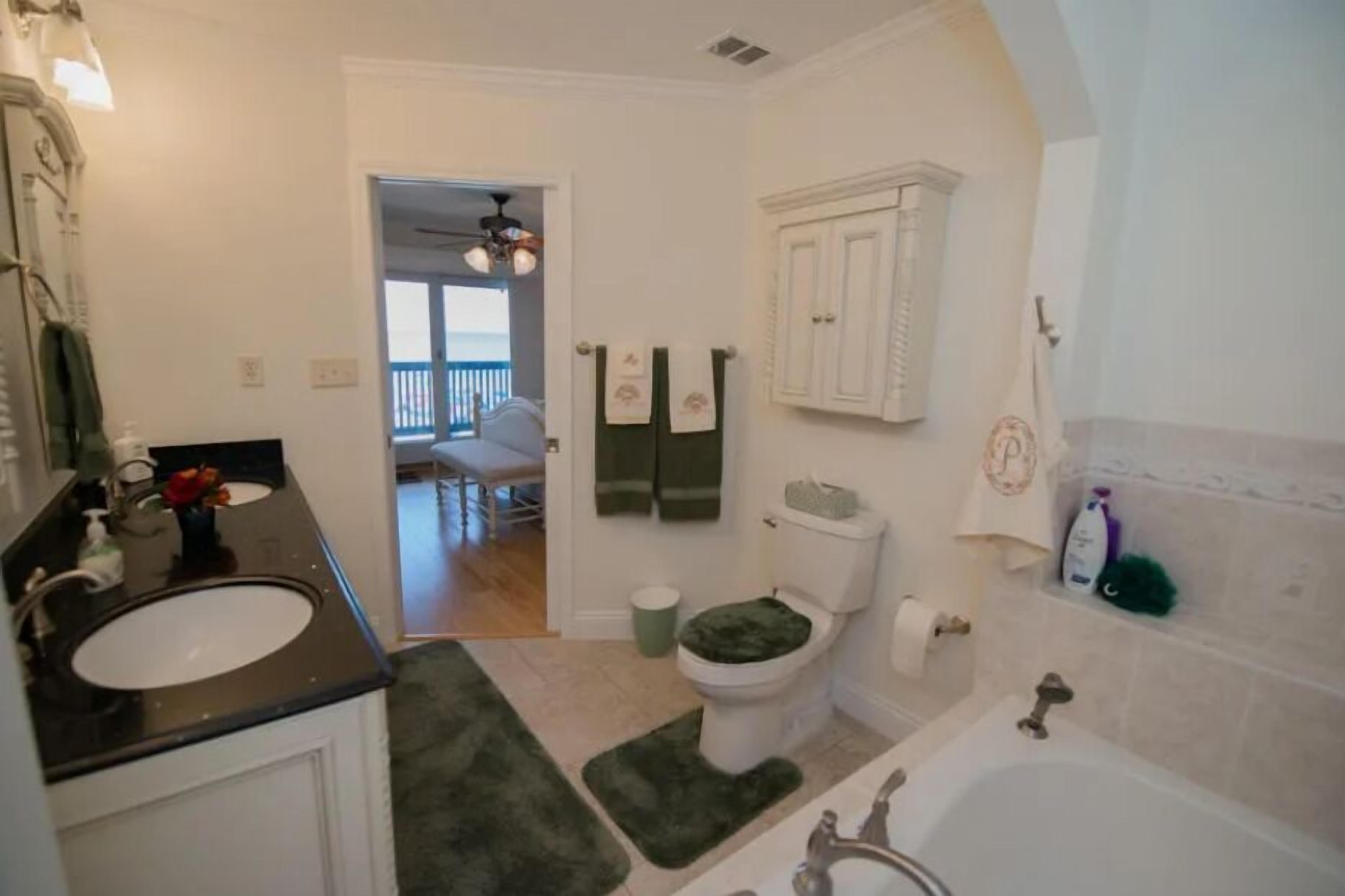 Casa de banho com lavatório, sanita e banheira. Há um tapete verde no chão e um porta-toalhas acima da sanita.