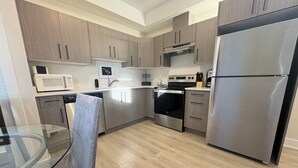 A modern kitchen with stainless steel appliances, wooden cabinets, and a glass dining table.