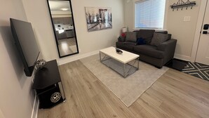 A modern living room with a flat-screen TV, a sofa, a coffee table, and a patterned rug.