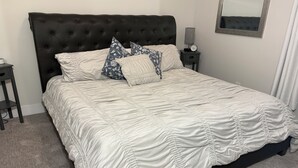 A neatly made bed with a tufted headboard, a white quilt, and patterned pillows.