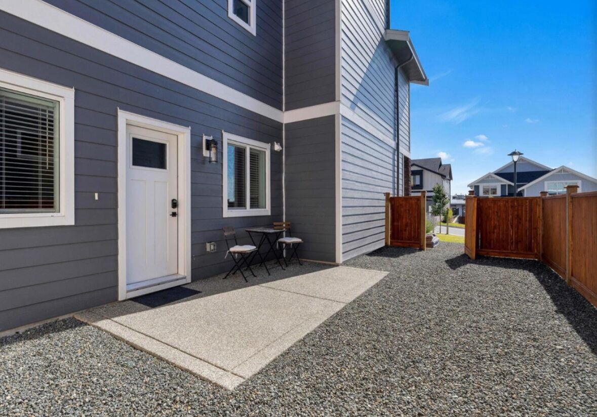A residential building with a grey exterior, a white door, and a small patio area with a table and chairs.