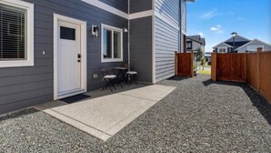 A residential building with a grey exterior, a white door, and a small patio area with a table and chairs.