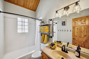 Ein Badezimmer mit einer Badewanne, Toilette, Waschtisch und einem Spiegel. Auf dem Waschtisch liegen Handtücher und Toilettenartikel.