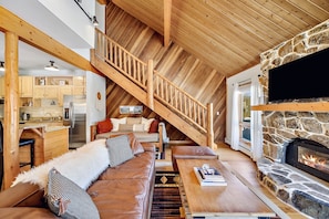 A cozy loft-style living area with a stone fireplace, wooden ceiling, and a staircase leading to an upper level. - Rustic chalet near skiing & trails (Silverthorne)