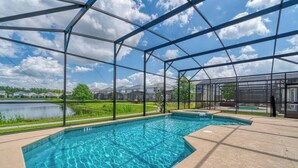 A swimming pool with a clear blue water feature, surrounded by a covered area with a metal frame and glass panels, overlooking a grassy area and a body of water.