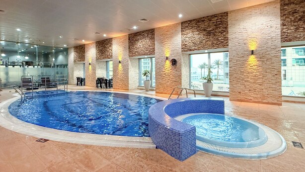 Une piscine intérieure avec un espace carrelé de carreaux bleus, des sièges disposés autour de la piscine et de grandes fenêtres offrant une vue panoramique.