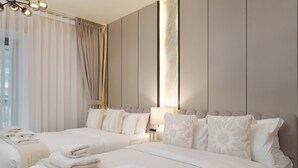 Une chambre d’hôtel avec deux lits, une grande fenêtre avec des rideaux légers, une lampe fixée au mur et une table de chevet avec un lampadaire.