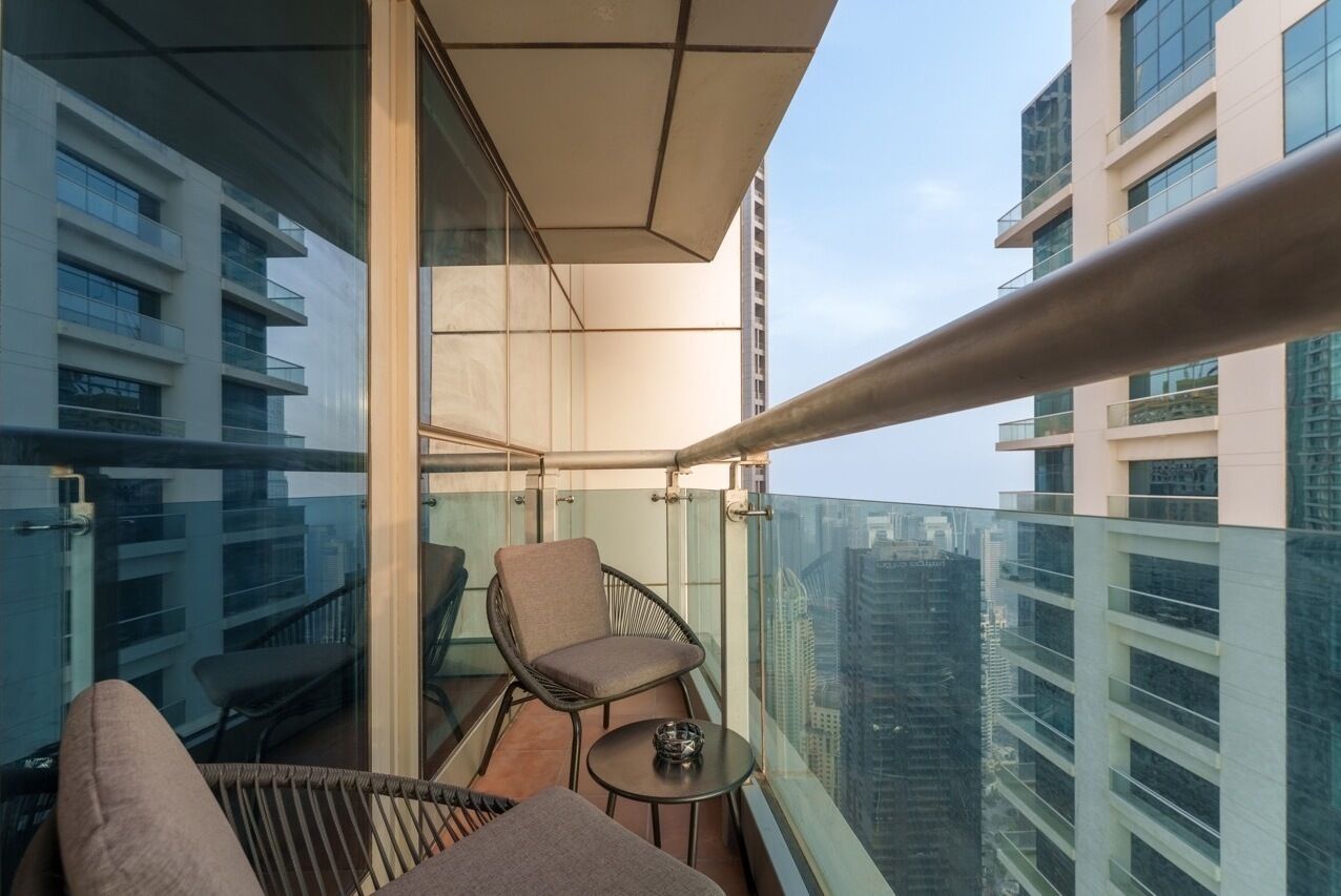 Un balcon doté d’une rambarde en verre, d’un fauteuil confortable, d’une petite table et offrant une vue sur les immeubles environnants.