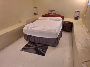 A bedroom with a bed, a nightstand, a wall-mounted artwork, and a tiled floor.