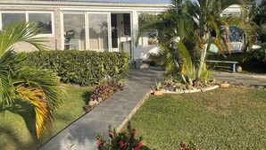 Ein modernes Haus mit einem gepflasterten Weg, der zum Eingang führt, umgeben von gepflegten Gärten und Palmen.