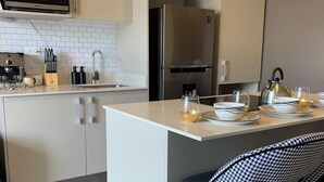 A modern kitchen with white cabinetry, a stainless steel refrigerator, a microwave, and a coffee machine. There is a bar area with stools and a kettle. - Executive studio close to National Stadium and AirPort (Rohrmoser)