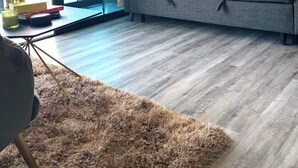 A modern living room with a grey sofa, a brown shag rug, and a glass door leading to an outdoor area. - Executive studio close to National Stadium and AirPort (Rohrmoser)