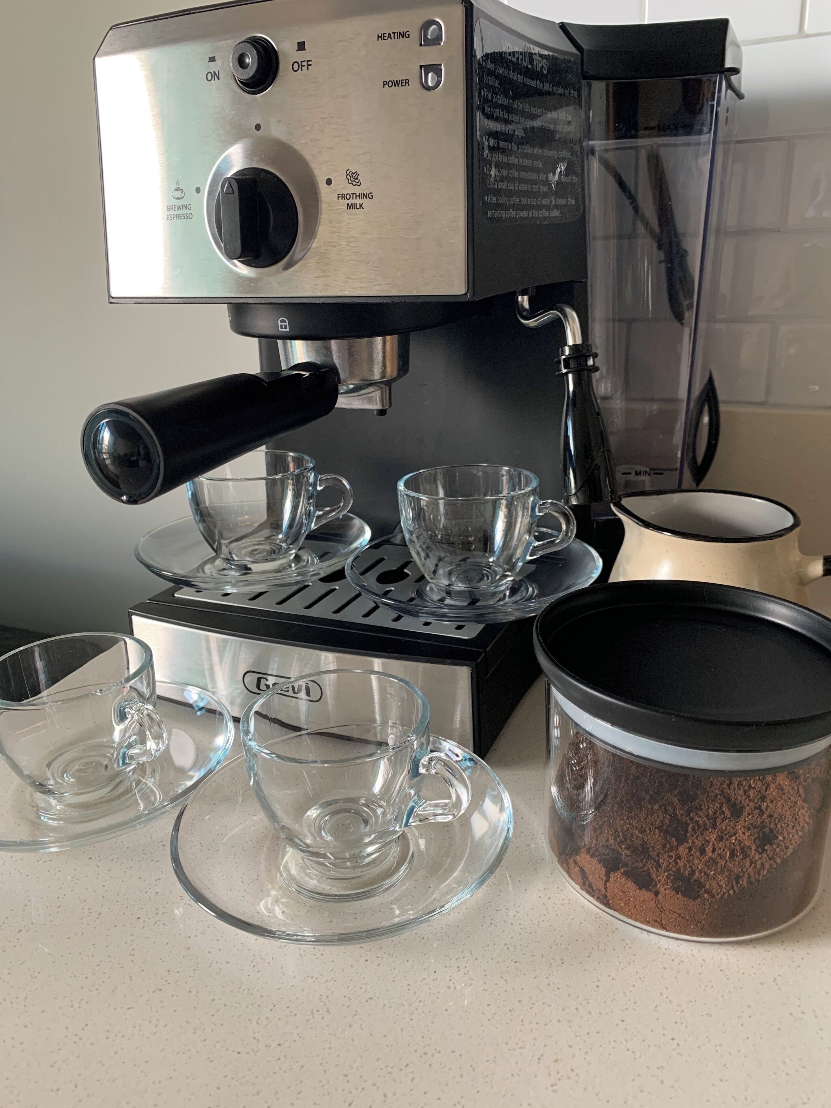 A coffee machine with a frothing milk button, a brewing espresso button, and a power button. There are four clear glass cups on the machine's drip tray.