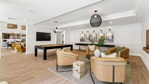 Ein modernes Wohnzimmer mit Billardtisch, bequemen Sitzgelegenheiten und einem Essbereich, der durch einen offenen Durchgang erreichbar ist.
