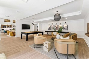 Ein modernes Wohnzimmer mit Billardtisch, bequemen Sitzgelegenheiten und einem Essbereich, der durch einen offenen Durchgang erreichbar ist.