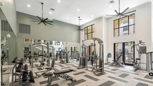 Ein geräumiger Fitnessraum mit verschiedenen Trainingsgeräten, großen Spiegeln und einem gemusterten Boden.