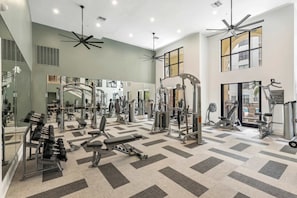Ein geräumiger Fitnessraum mit verschiedenen Trainingsgeräten, großen Spiegeln und einem gemusterten Boden.