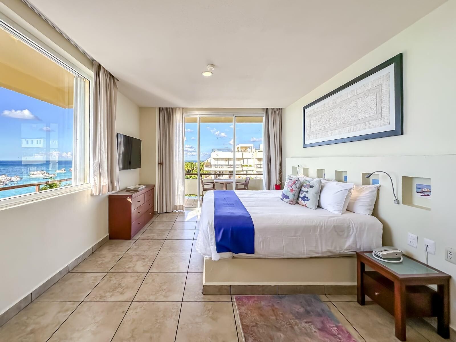 Habitación de hotel con cama, escritorio, televisión y balcón con vista al mar.