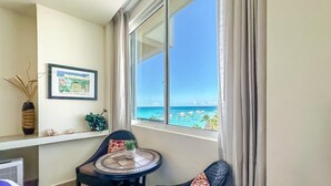 Un balcon donnant sur la mer, une chaise, une petite table ronde et un tableau encadré accroché au mur.