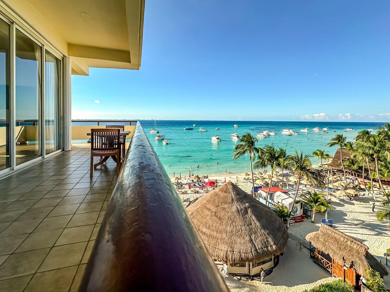 A balcony with a view of a beach, palm trees, and boats.