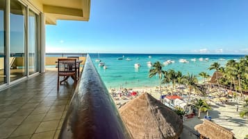A balcony with a view of a beach, palm trees, and boats.