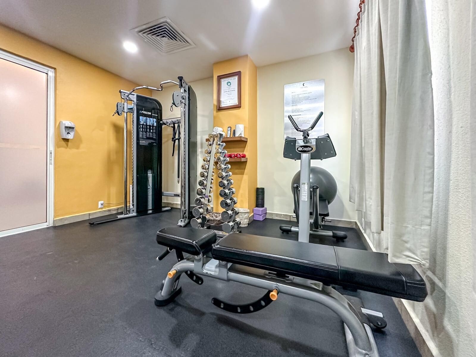 Ein Fitnessstudio mit Hantelbank, Kurzhanteln und Cardiogeräten.