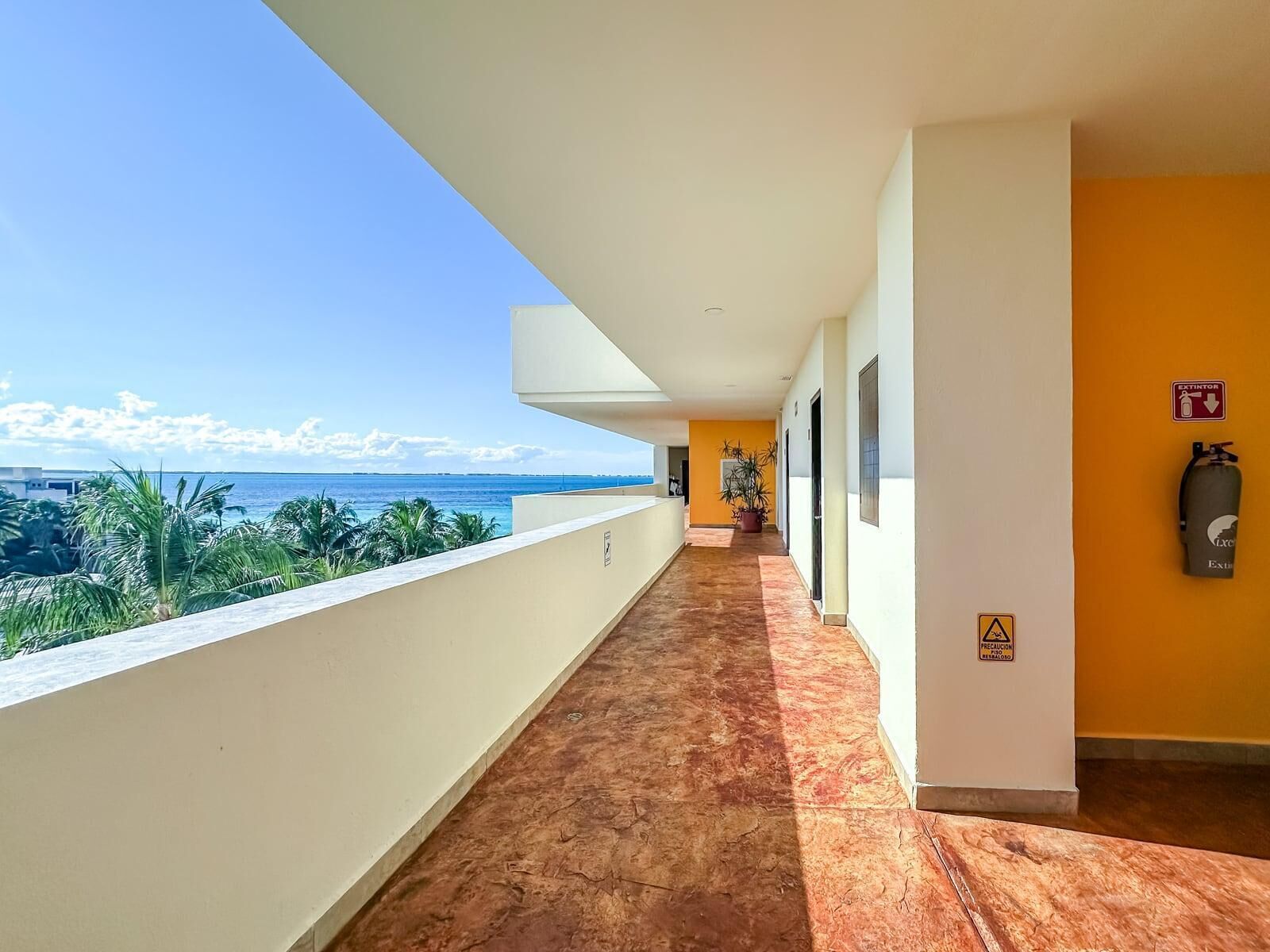 A corridor with a view of the ocean, a fire extinguisher, and a caution sign.