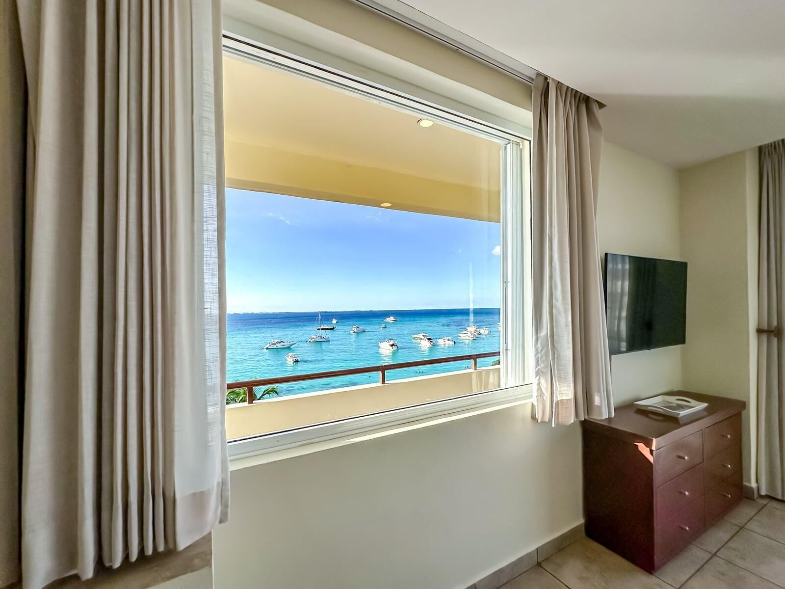 A room with a large window offering a view of the sea and boats.