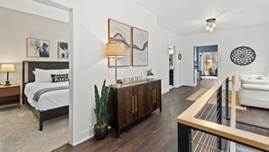 Une chambre d’hôtel moderne, avec un lit, une armoire en bois, une plante en pot et des œuvres d’art accrochées aux murs.