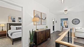 Une chambre d’hôtel moderne, avec un lit, une armoire en bois, une plante en pot et des œuvres d’art accrochées aux murs.