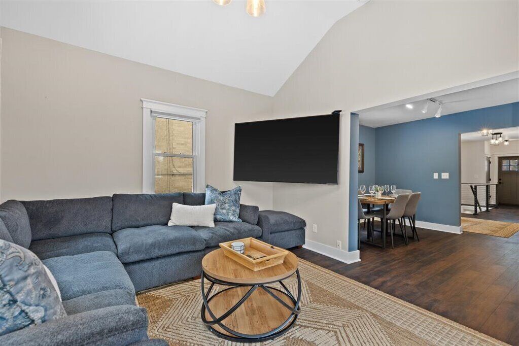 A modern living room with a sectional sofa, a round coffee table, and a flat-screen TV mounted on the wall.