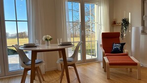 Un comedor con una mesa dispuesta para cuatro, dos sillas y vistas a un campo a través de amplios ventanales.