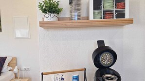 Una sala de estar moderna con una cama, una cafetera y un estante con una planta y recipientes de almacenamiento.