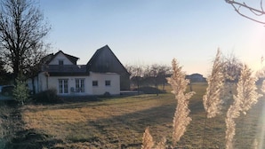 Una casa con techo inclinado y porche delantero, rodeada de un campo cubierto de césped y árboles.