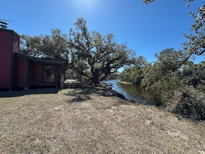 A riverside cabin with a deck, surrounded by trees and a clear sky.