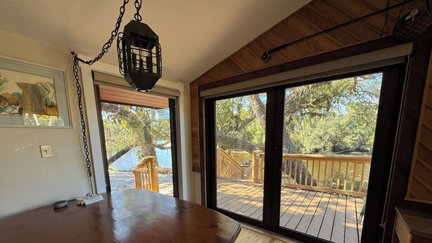 Una mesa de comedor de madera con un banco, un farol colgante y vistas a una terraza de madera y árboles a través de grandes puertas corredizas de vidrio.