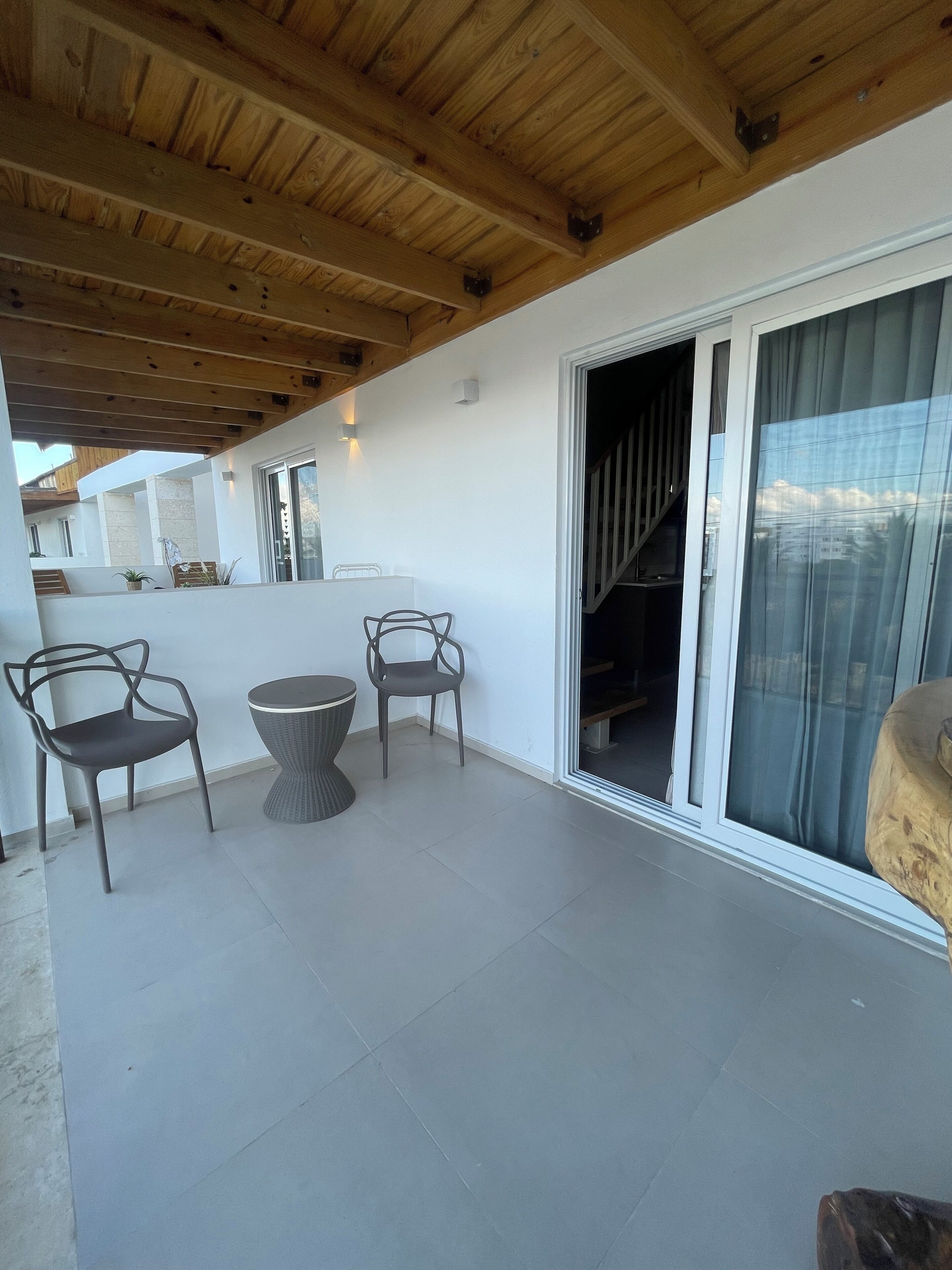 Un patio couvert doté d’un plafond en bois, d’une table avec des chaises et d’une porte-fenêtre coulissante donnant sur un escalier.