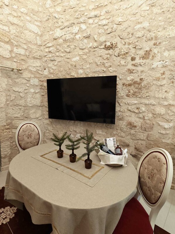 A round table with a beige tablecloth, two chairs with patterned upholstery, a small potted plant, a bottle, and a white basket with a newspaper. - Suite Napoléon: Comfort, Bed 200x200, Heated pool DOMAINE DE PAGNON GIRONDE (Saint-Gervais)